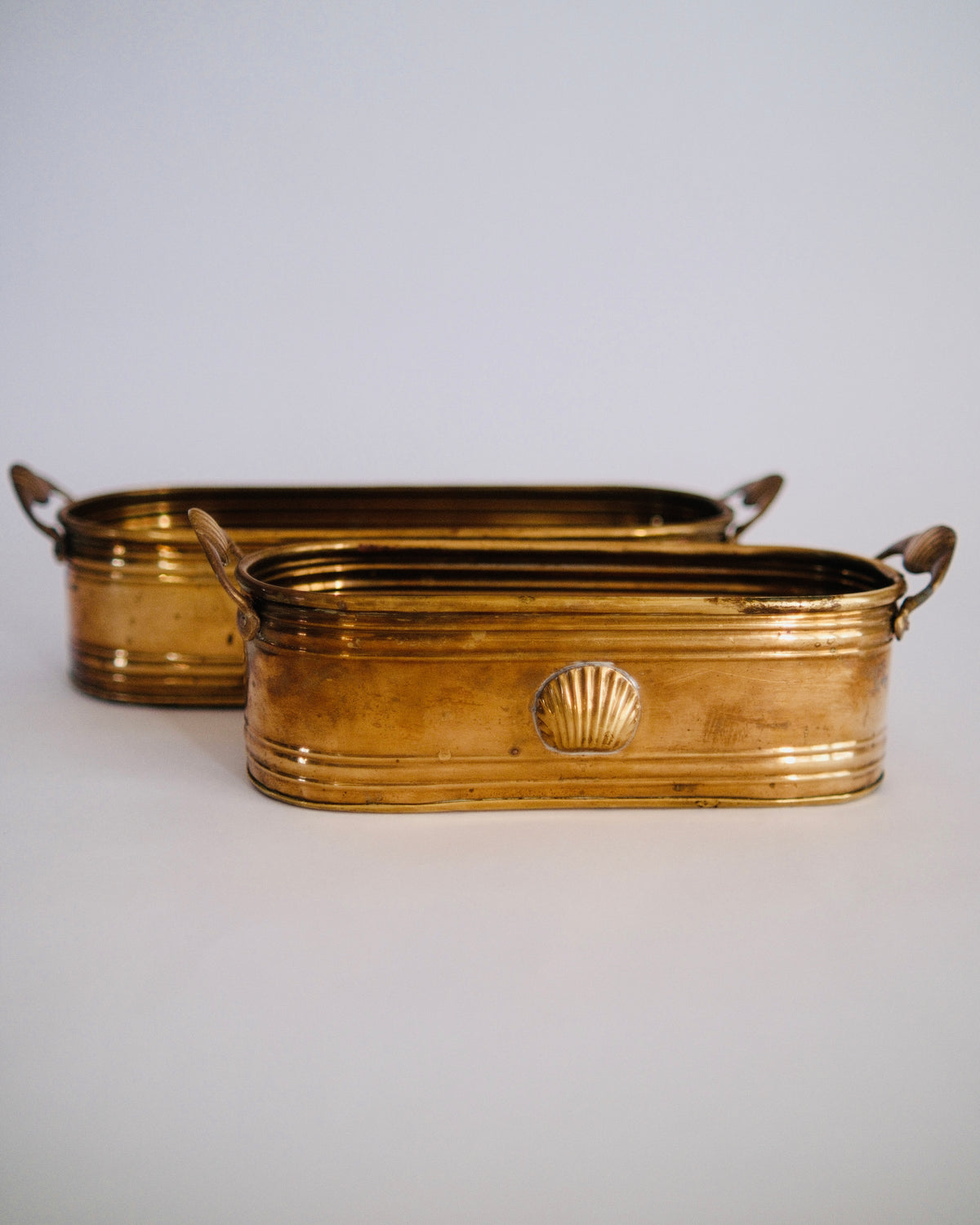 Detail of vintage oval brass planter trough showing raised seashell emblem and rich aged patina - Eulogy Vintage